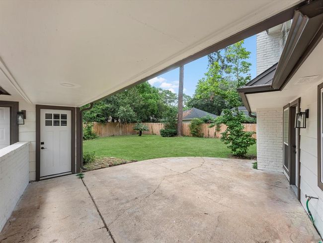 This photo showcases a covered patio area leading to a spacious, fenced backyard with lush greenery, perfect for outdoor activities and relaxation. | Image 37