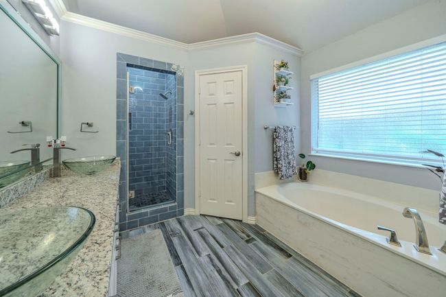 Bathroom with a garden tub, double vanity, a shower stall, wood finished floors, and crown molding | Image 14