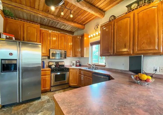 Kitchen featuring stainless steel appliances, a wood ceiling with exposed beams, brown cabinetry, and track lighting | Image 15