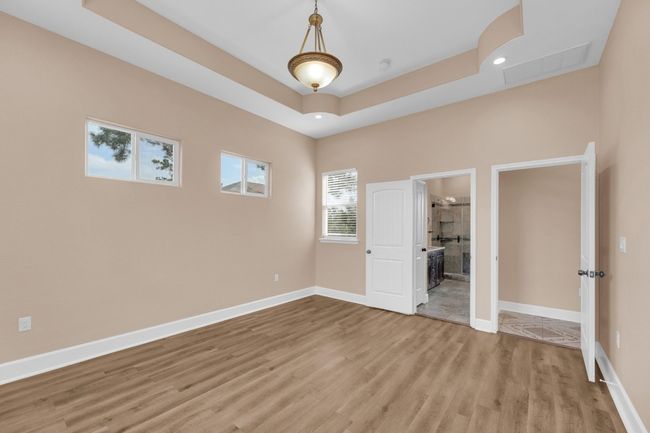 Unfurnished bedroom with a tray ceiling, wood finished floors, a fireplace, recessed lighting, and ensuite bathroom | Image 17