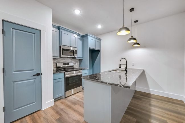 Kitchen with dark stone countertops, a peninsula, light wood-style flooring, appliances with stainless steel finishes, and a sink | Image 8