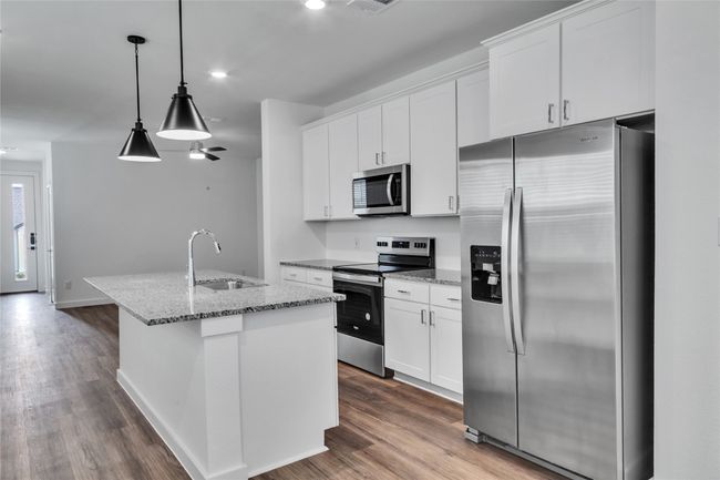 Kitchen with dark wood-style flooring, appliances with stainless steel finishes, white cabinets, a sink, and an island with sink | Image 4