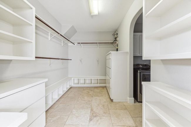 Spacious walk-in closet with ample shelving, hanging rods, and built-in storage. It features tile flooring and an open archway leading to an adjacent laundry area. | Image 20