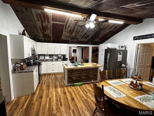 Kitchen with ceiling fan, fridge with ice dispenser, white cabinetry, black range with electric cooktop, and vaulted ceiling with beams | Image 10