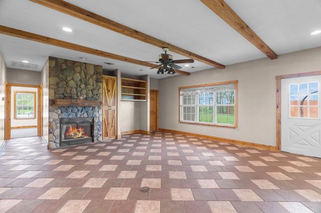 Unfurnished living room with ceiling fan, a fireplace, visible vents, baseboards, and beam ceiling | Image 21
