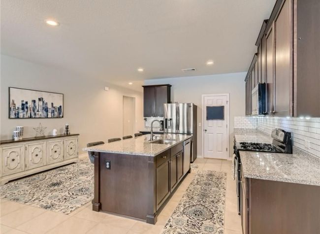 Kitchen with appliances with stainless steel finishes, backsplash, light stone counters, dark brown cabinetry, and a kitchen island with sink | Image 12
