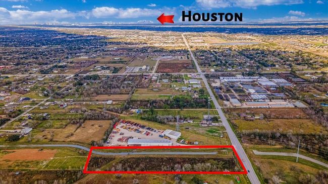 The photo shows a spacious plot of land outlined in red, located in a suburban area with a view toward Houston in the distance. It's surrounded by open fields, residential areas, and accessible roads, offering both tranquility and connectivity. | Image 18