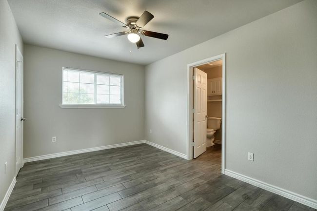 Unfurnished bedroom with dark wood-style floors, ensuite bath, and ceiling fan | Image 10