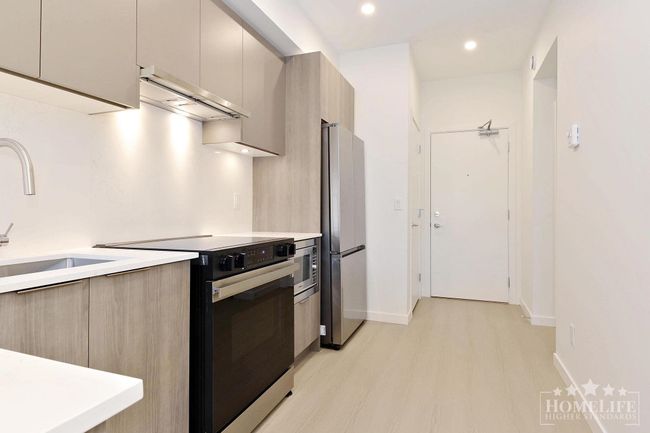 Kitchen featuring a sink, light wood-type flooring, light countertops, appliances with stainless steel finishes, and ventilation hood | Image 7