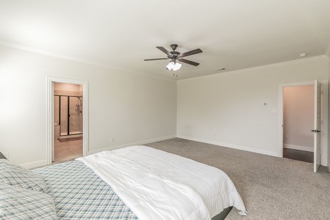 Bedroom featuring a ceiling fan, baseboards, ensuite bath, crown molding, and light colored carpet | Image 27