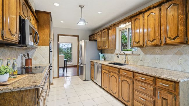 Kitchen featuring a sink, light stone counters, pendant lighting, stainless steel appliances, and brown cabinetry | Image 12