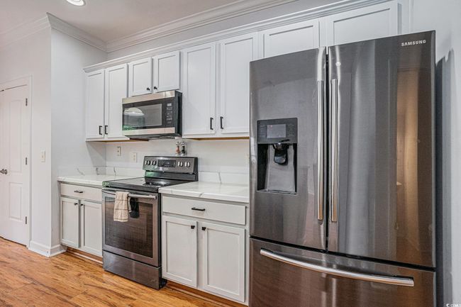 Kitchen with appliances with stainless steel finishes, crown molding, light wood-type flooring, white cabinetry, and light stone counters | Image 5