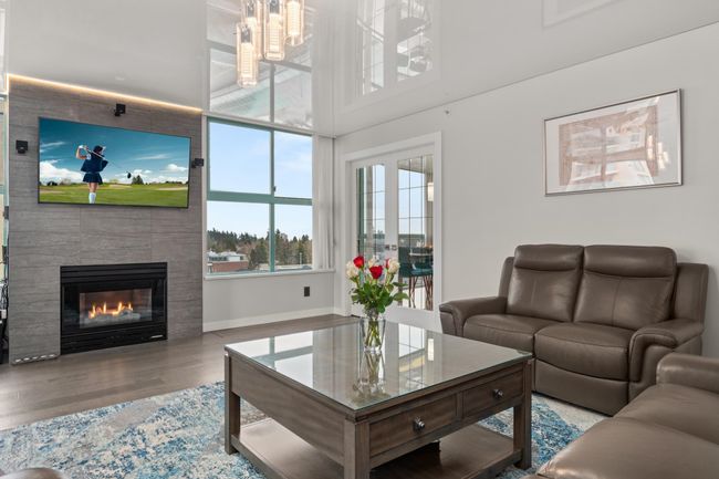 Living room with baseboards, a high ceiling, a large fireplace, and wood finished floors | Image 13