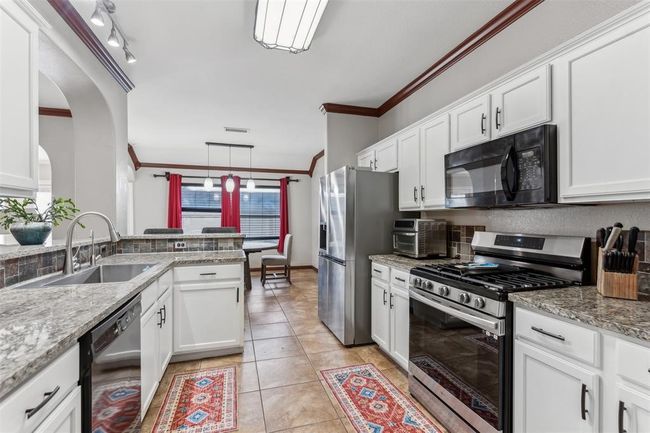 Kitchen featuring black appliances, crown molding, light tile patterned flooring, white cabinetry, and a sink | Image 10