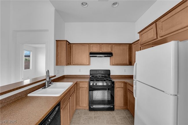 Kitchen featuring a sink, brown cabinetry, black appliances, under cabinet range hood, and recessed lighting | Image 7
