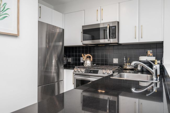 Kitchen with white cabinetry, tasteful backsplash, appliances with stainless steel finishes, dark countertops, and light wood-style floors | Image 10