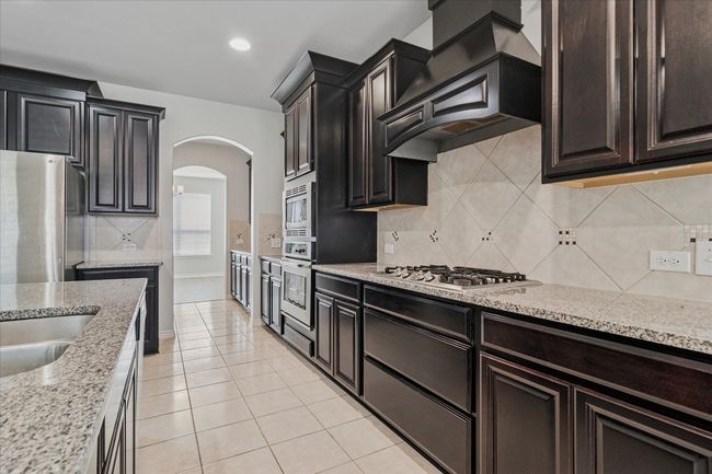 Kitchen with custom exhaust hood, light tile patterned flooring, arched walkways, stainless steel appliances, and tasteful backsplash | Image 12
