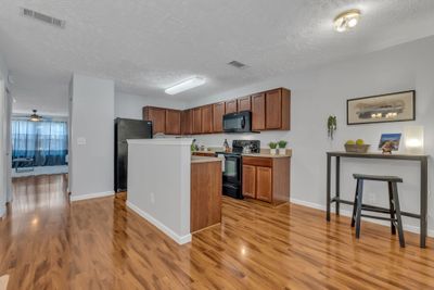 View from the back door entrance. Laminate flooring is continuous. Sink and dishwasher are in the island. Lots of cabinets. Pantry and coat closet in passage to the living room. Powder room is there on the left just out of sight. | Image 3