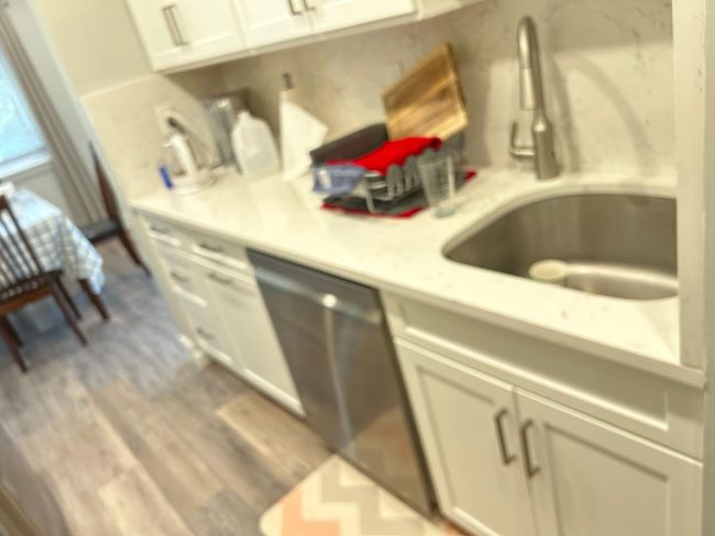 Kitchen featuring a sink, dishwasher, light countertops, wood finished floors, and white cabinetry | Image 13