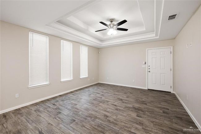 Empty room featuring a raised ceiling, a ceiling fan, and dark wood finished floors | Image 7