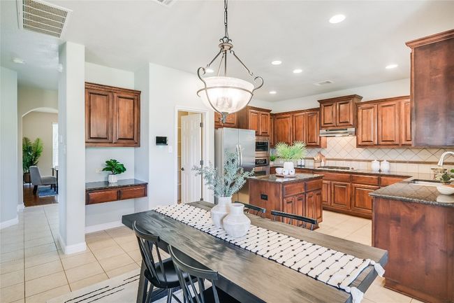 Kitchen with arched walkways, light tile patterned floors, recessed lighting, a center island, and stainless steel fridge with ice dispenser | Image 7