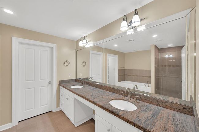 Gorgeous multi color stone countertops of Primary Bath has two undermount sinks with replaced plumbing fixtures. Nice storage in cabinetry with open vanity seating space. You can see the glass enclosure of the shower beside jetted soaking tub in mirror reflection. | Image 23