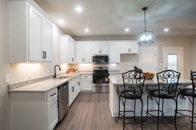 Kitchen featuring appliances with stainless steel finishes, a sink, a breakfast bar area, white cabinets, and recessed lighting | Image 12