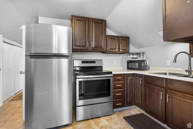 Kitchen with dark brown cabinets, vaulted ceiling, appliances with stainless steel finishes, light countertops, and a sink | Image 13