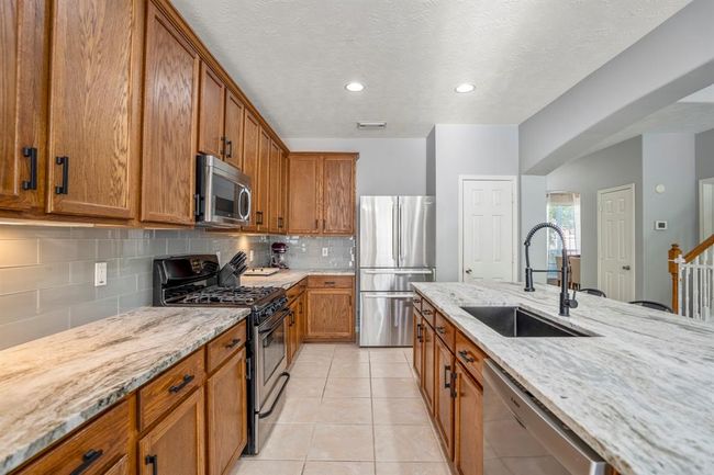 From the breakfast area, this view highlights the kitchen’s gorgeous leathered granite counters, stainless appliances, tall upper cabinets, and under-cabinet lighting. Straight ahead is the refrigerator with the pantry just beside it. To the right, you’ll spot the formal dining room through the arched opening in the distance and a convenient hall closet for extra storage. | Image 13
