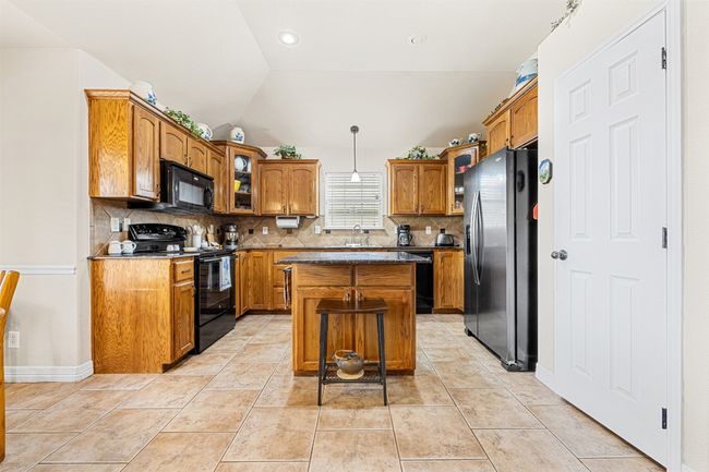 Kitchen with black appliances, decorative backsplash, brown cabinetry, a kitchen island, and vaulted ceiling | Image 11