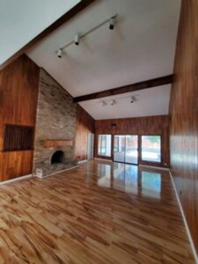 Unfurnished living room with wooden walls, wood finished floors, beamed ceiling, a fireplace, and high vaulted ceiling | Image 7