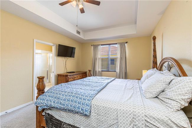 Carpeted bedroom with ensuite bathroom, a ceiling fan, visible vents, a raised ceiling, and baseboards | Image 18