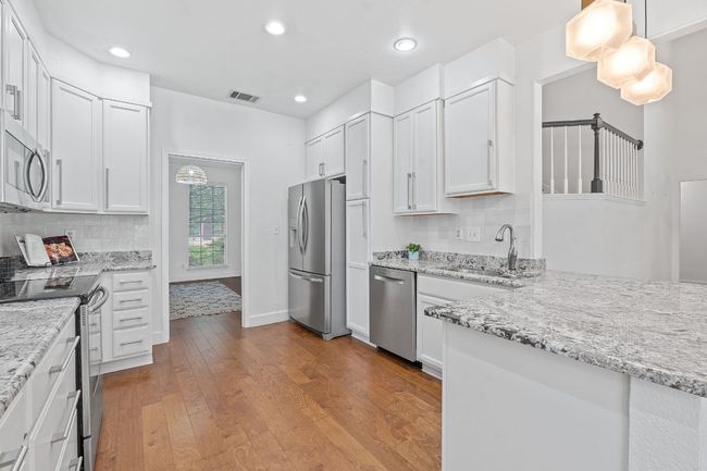 Kitchen with stainless steel appliances, wood finished floors, white cabinets, light stone countertops, and recessed lighting | Image 9