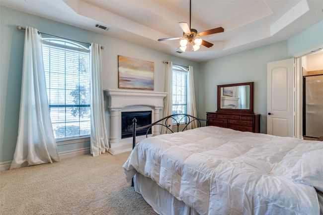 Bedroom featuring visible vents, a fireplace with raised hearth, a raised ceiling, and carpet | Image 24