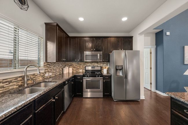 Kitchen featuring appliances with stainless steel finishes, a sink, backsplash, dark wood-style floors, and dark stone counters | Image 12