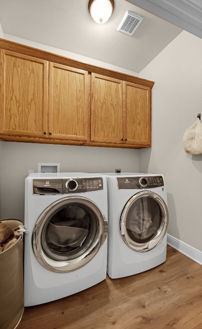 Washroom featuring washing machine and dryer, visible vents, wood finished floors, and cabinet space | Image 30