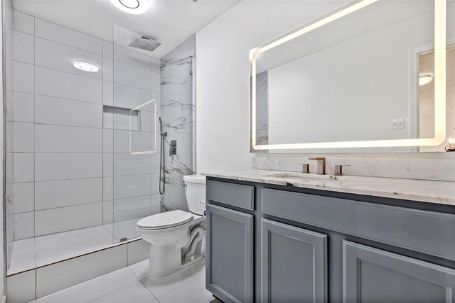 Modern bathroom featuring a spacious glass-enclosed shower, elegant marble-style tiles, a sleek vanity with ample storage, and a large illuminated mirror. | Image 25