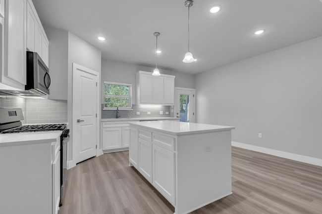 Kitchen with light countertops, stainless steel gas range, baseboards, light wood-style floors, and a center island | Image 10