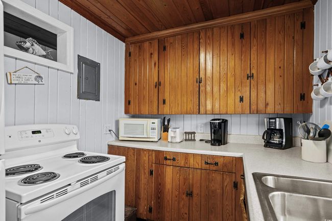 Kitchen featuring white appliances, wooden ceiling, electric panel, brown cabinets, and light countertops | Image 19