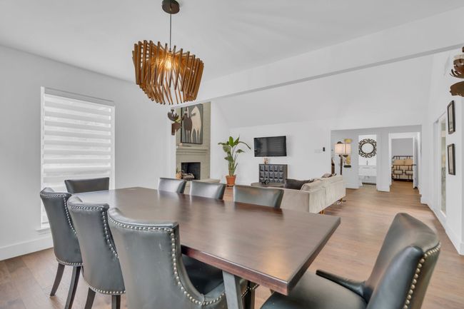 Dining area featuring a notable chandelier, a large fireplace, baseboards, wood finished floors, and lofted ceiling | Image 14
