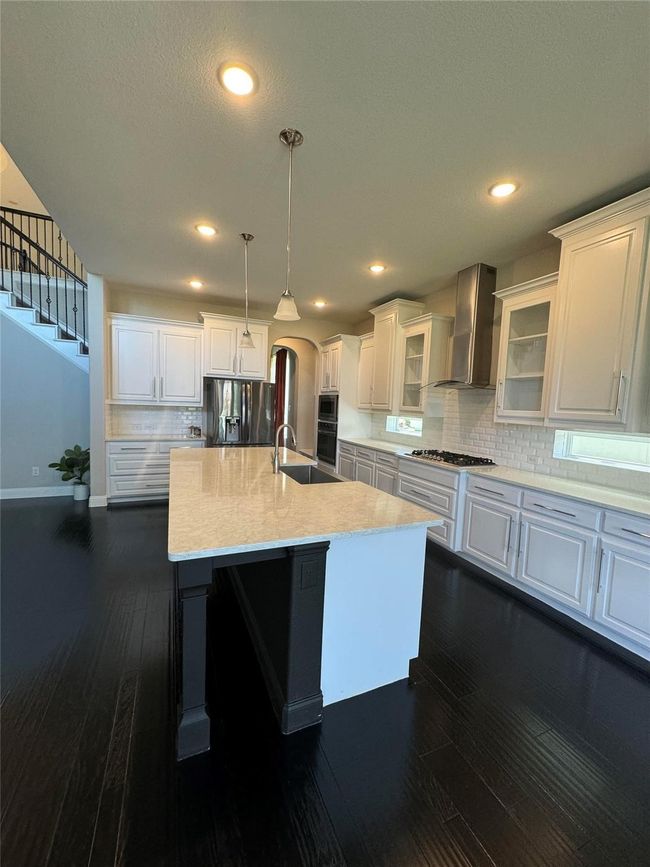 Kitchen with wall chimney range hood, refrigerator with ice dispenser, dark wood-style flooring, white cabinetry, and recessed lighting | Image 20