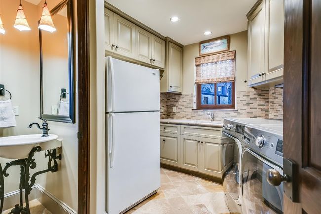 Kitchen with a sink, freestanding refrigerator, cream cabinets, washer and dryer, and decorative backsplash | Image 39