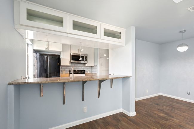 Kitchen featuring light stone counters, a peninsula, decorative backsplash, black appliances, and a kitchen bar | Image 7