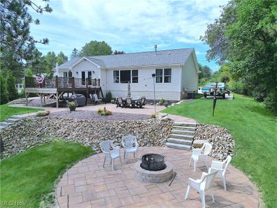 Back of property with a lawn, a deck, a patio, and an outdoor fire pit | Image 1