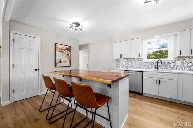 Kitchen featuring stainless steel dishwasher, a breakfast bar, light wood-style flooring, and backsplash | Image 10