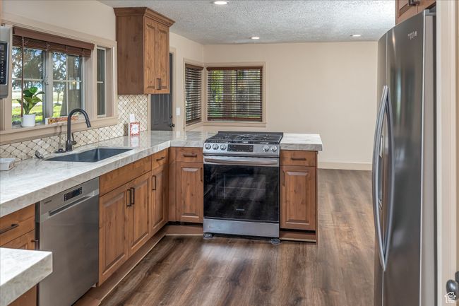 Kitchen with stainless steel appliances, brown cabinetry, a peninsula, light countertops, and a textured ceiling | Image 18