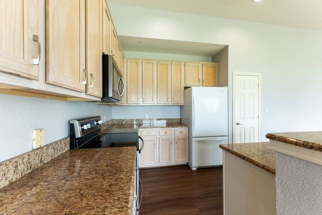 Kitchen with stainless steel appliances, dark wood-style flooring, dark stone countertops, and light brown cabinetry | Image 13