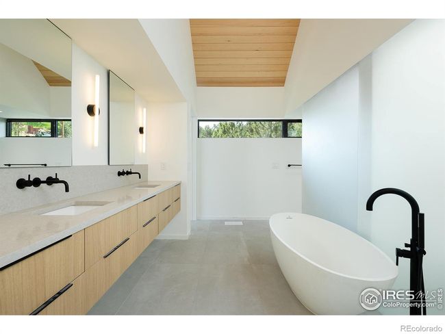 Luxurious primary bathroom with solid stone freestanding soaking tub, walk-ins shower withe expansive skylight above, custom oak floating vanity with two sinks, wall mount plumbing fixtures and toilet , large format tile throughout | Image 22