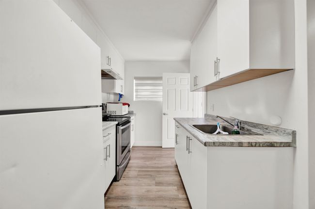 Kitchen with freestanding refrigerator, a sink, stainless steel electric range oven, under cabinet range hood, and white cabinetry | Image 10