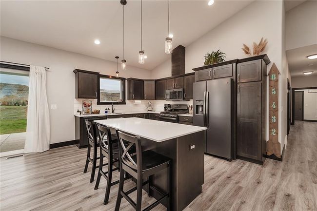 Pendant lighting above quartz countertops at the large island, black smoky finish over alder cabinets and trim.Four ft hall way off the Freat room to bedrooms and bath. | Image 8